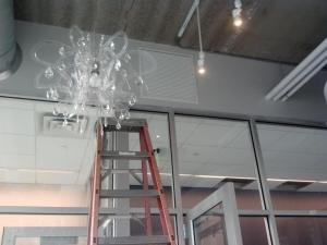 Chandelier next to a tall step ladder, suspended from a partially complete ceiling.